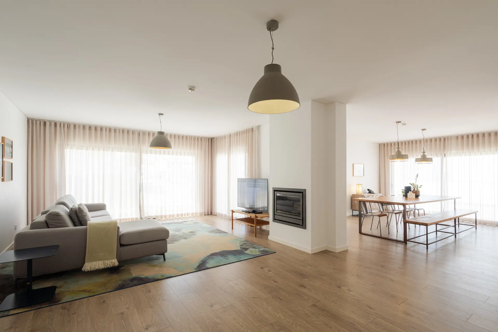 Sala de um apartamento com lareira, sofá e mesa de jantar, com luz natural