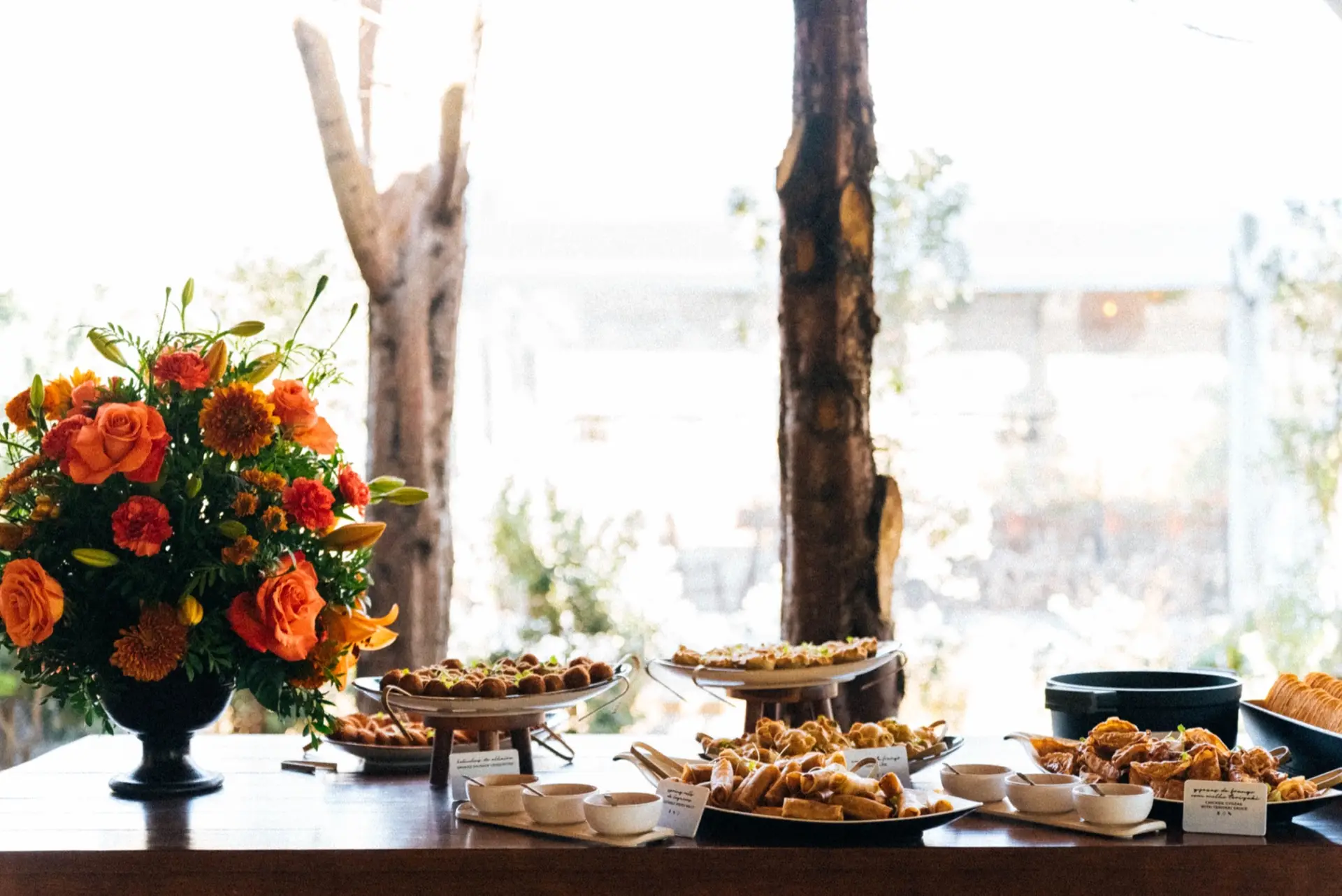 Mesa de buffet com várias travessas e arranjos de flores cor de laranja